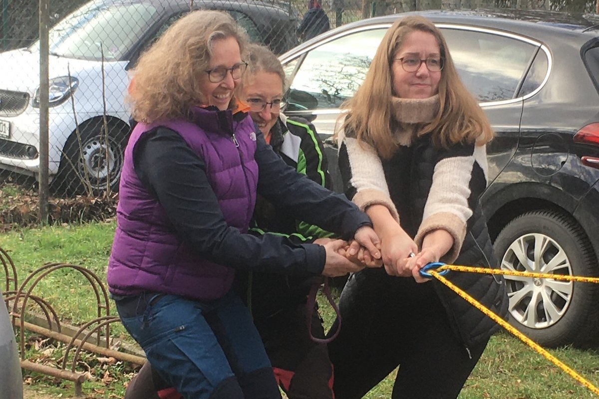 Zu dritt wird versucht, ein nicht im Bild gezeigtes Auto, mit Hilfe eines Flaschenzugs zu ziehen